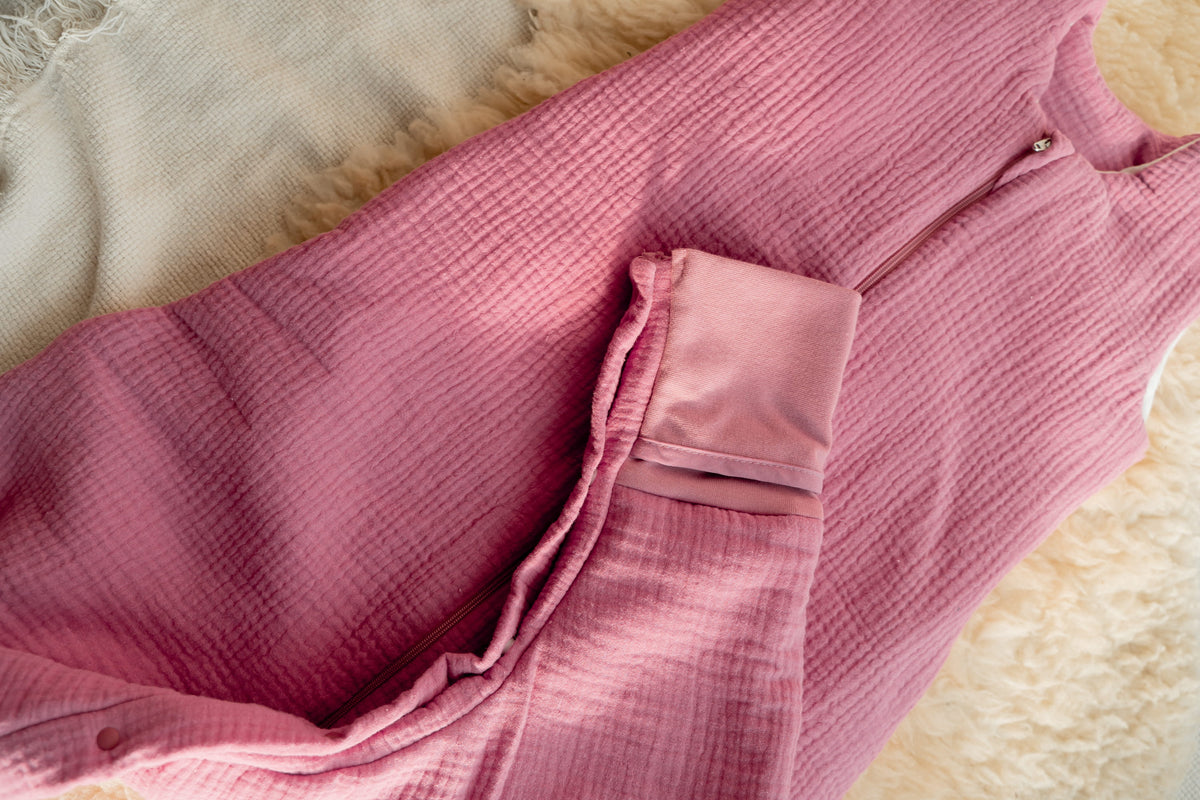 Rosa Baby-Schlafsack aus weichem Musselin-Stoff mit seitlichem Reißverschluss, liegend auf einer cremefarbenen Fell- und Decke-Unterlage